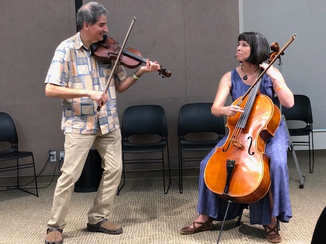 a man playing the fiddle and a woman playing the cello at the library